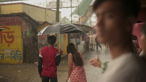 Boy-comes-with-umbrella-and-lets-a-girl-come-under-his-umbrella-and-walk-away-in-rain,-People-stuck-in-rain,-monsoon-season,-slow-motion-shot-of-rain-drops