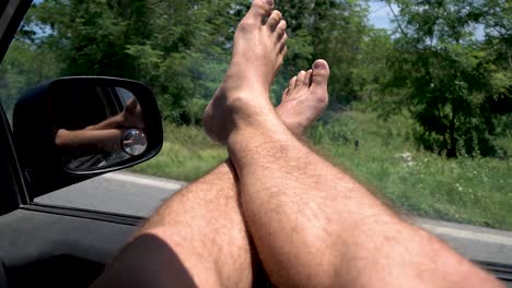 Male-legs-hanging-out-from-car-window-in-the-west-coast-with-motorcycle-rider-passing,-Through-window-shot
