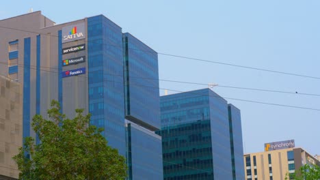 Logotipos-De-Sattva,-Servicenow,-Microsoft-Y-Fanáticos-En-Edificios-Rascacielos-En-El-Distrito-Comercial,-Financiero-Y-De-Negocios-Del-Centro-De-La-Ciudad