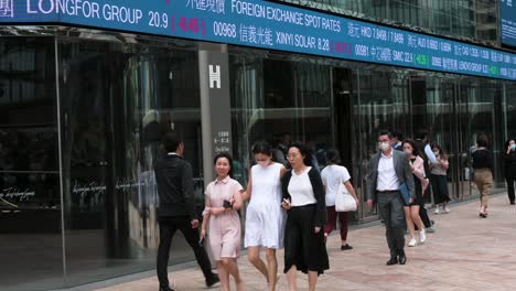 Pedestrians-walk-past-an-electronic-ticker-board-and-screen-displaying-stock-market-figures-outside-the-Exchange-Square-complex,-which-houses-the-Hong-Kong-Stock-Exchange