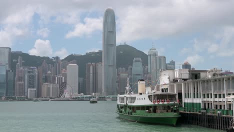 A-Star-Ferry-docked-at-a-waterfront-ferry-terminal-pier-on-Hong-Kong's-Victoria-Harbour-as-the-Hong-Kong-skyline-is-seen-in-the-background