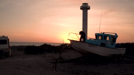 Lighthouse-with-fisherman-tending-boat-at-sunset-in-western-Baja,-Wide-shot