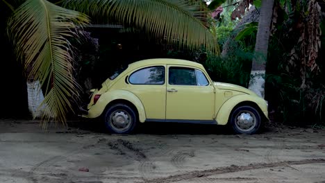 Klassisches-Gelbes-VW-Käferauto,-Das-Im-Sand-In-Der-Nähe-Des-Strandes-Geparkt-Ist-Und-Auf-Dem-Sockel-Aufsteigt