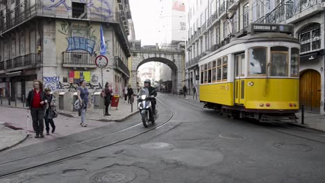 A-yellow-tram-arrives-at-Cais-Sodre,-in-the-center-of-Lisbon,-Portugal,-as-people-walk-by