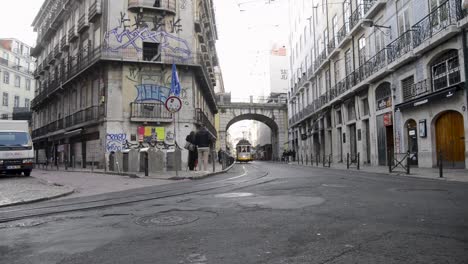 A-yellow-tram-arrives-at-Cais-Sodre,-in-the-center-of-Lisbon,-Portugal,-as-people-walk-by