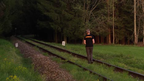 Young-man-with-a-camera-in-his-hand-walks-slowly-along-the-tracks-in-the-forest-on-a-sunny-sunset-evening