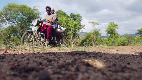 Two-guys-on-a-bike-passing-by-on-a-dirt-road-in-the-African-Savanna-in-Ethiopia-Omo-Valley-region