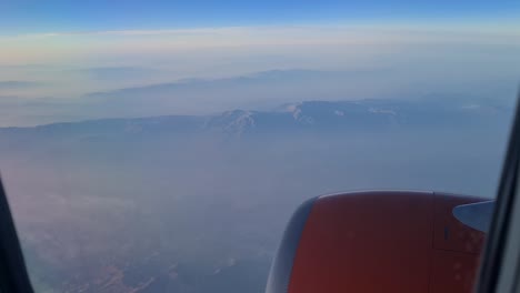 Vista-Desde-La-Ventana-Del-Avión-Sobre-El-Motor-A-Reacción,-Al-Fondo-Podemos-Ver-Nubes,-Tierra-Y-Montañas