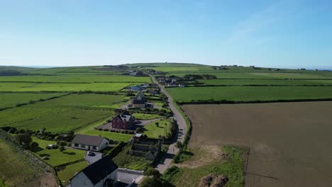 Hyperlapse-on-a-sunny-day-an-aerial-over-green-fields-and-village-road-with-houses-near-Old-Head,-Kinsale-Ireland