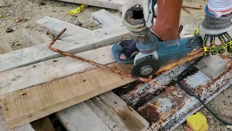 Manual-worker-with-grinder-bosch-tool-to-cut-rusty-iron-rod-with-sparks-flying,-close-up