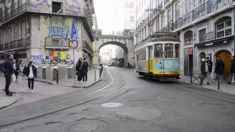 A-yellow-tram-goes-by-Cais-Sodre,-in-the-center-of-Lisbon,-Portugal,-as-people-walk-by