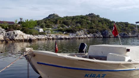 Pequeño-Barco-En-El-Puerto-De-Simena-Con-Bandera-Turca-Con-El-Castillo-En-Segundo-Plano.