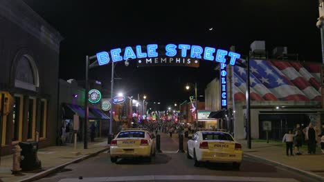 Cartel-De-La-Calle-Beale-En-Memphis,-Tennessee,-De-Noche,-Con-Dos-Coches-De-Policía-Y-Un-Vídeo-De-Cardán-Caminando-Hacia-Adelante