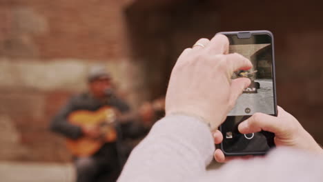 Persona-Acercándose-A-Un-Músico-Callejero-En-Un-Teléfono-Inteligente-Tomando-Fotos-En-Barcelona,-España