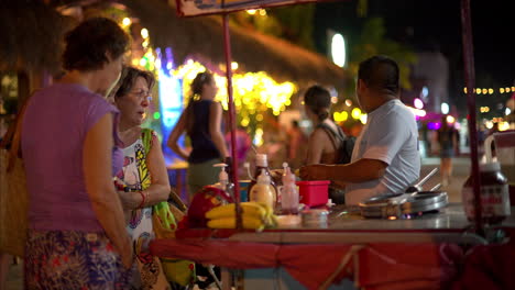 Latin-baby-boy-toddler-with-his-grandma,-mom-and-aunties-waiting-for-a-snack-typical-snack-Marquesitas-prepared-on-the-streets-of-downtown-Isla-Mujeres-Cancun-Mexico