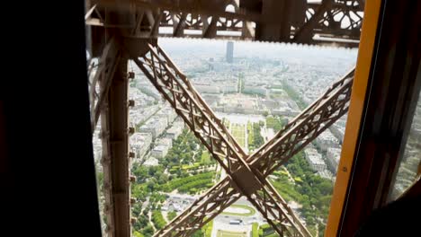 Handheld-camera-shot-inside-the-Eiffel-Tower-elevator-ascending-with-the-Champ-de-Mars-in-the-background,-Paris,-France