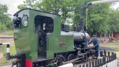 Man-dressed-as-a-stationmaster-refilling-the-locomotive-of-a-vintage-steam-train-with-water
