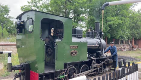 Hombre-Vestido-Como-Jefe-De-Estación-Rellenando-Con-Agua-La-Locomotora-De-Un-Tren-De-Vapor-Antiguo