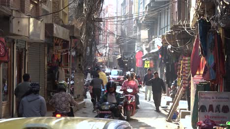 Toma-De-Tráfico-En-Una-Pequeña-Calle-De-Katmandú-Con-Autos-Y-Nepaleses-Caminando-Nepal