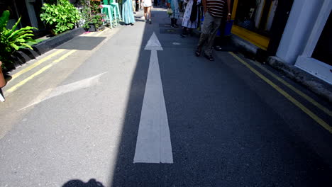 A-large-white-directional-arrow-on-the-road-with-sunshine-and-shadow-on-each-side-and-people-walking