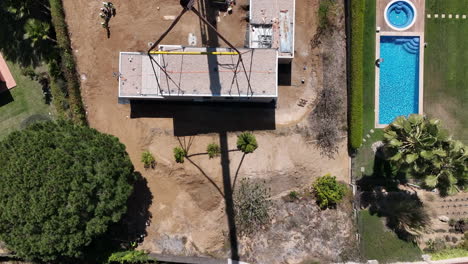 Constructing-modular-home-building-near-luxury-pool,-aerial-top-down-view