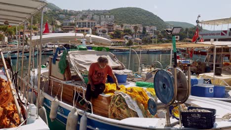 Pescador-Turco-Remendando-Sus-Redes-A-Bordo-De-Su-Barco-Que-Se-Balancea-En-El-Puerto-De-Kac