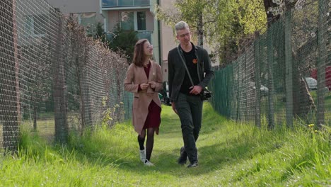 Couple-of-young-man-and-girl-walking-between-fences-on-green-spring-grass-in-sunny-spring