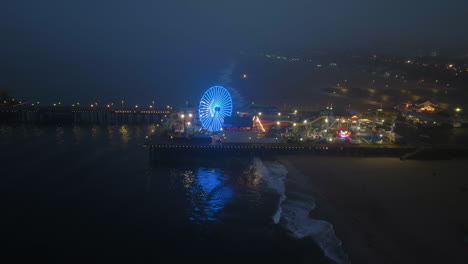 Aerial-view-tilting-over-the-Pacific-park-on-Santa-Monica-pier,-foggy-evening-in-LA,-USA