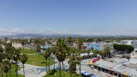 Restaurants-and-shops-at-the-Venice-boardwalk,-in-sunny-Los-Angeles,-USA---Ascending,-aerial-view