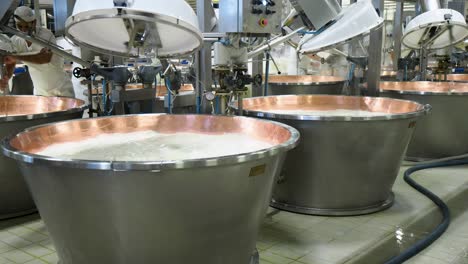 Parmesan-cheese-cooking-organic-milk,-whey-and-rennet-in-copper-cauldrons-,-worker-stirring-curd