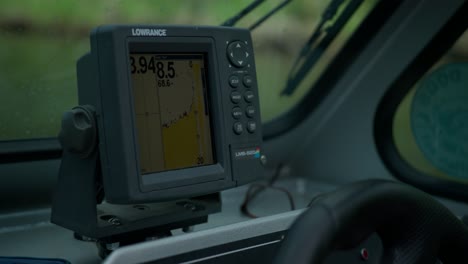 Close-up-of-depth-finder-or-fish-finder-with-GPS-on-fishing-boat-with-hand-on-steering-wheel-steering-boat