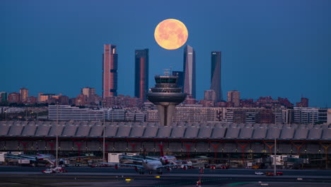 Full-moon-setting-behind-the-Four-Tower-and-International-Airport-in-Madrid,-Spain