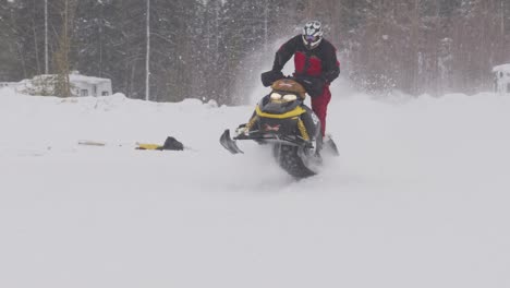 Der-Skidoo-Schneemobilrennfahrer-Läuft-In-Zeitlupe-über-Einen-Hügel,-Während-Der-Schnee-Weht