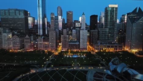Aerial-view-backwards-over-the-illuminated-Millennium-Park,-summer-morning-in-Chicago,-USA