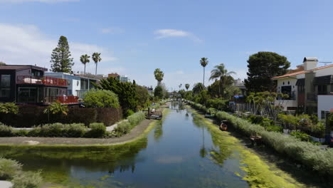 People-enjoying-a-warm,-sunny-day-at-the-waterway-in-the-Venice-neighborhood-of-Los-Angeles,-USA---Aerial-view