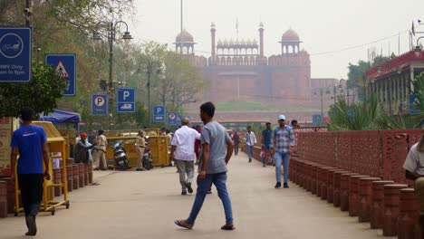 People-walking-at-the-street-of-newly-developed-Chandni-Chowk-in-old-Delhi,-view-of-historical-building-Lal-Quila-Red-Fort-in-background,-India