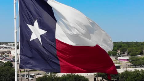 Eine-Nahaufnahme-Der-Texanischen-Flagge-Mit-Einem-Strahlend-Blauen-Himmel-Und-Einem-Blick-Auf-Die-Stadt-Wacos-Im-Hintergrund