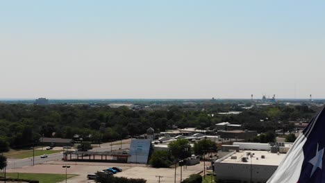Eine-Nahaufnahme-Der-Texas-Flagge-Mit-Einem-Strahlend-Blauen-Himmel-Und-Einem-Blick-Auf-Die-Stadt-Wacos-Im-Hintergrund