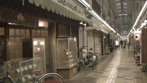 Leere-Einkaufspassage-In-Tokio-Mit-Vor-Dem-Laden-Geparkten-Fahrrädern---Menschen,-Die-In-Der-Ferne-Laufen