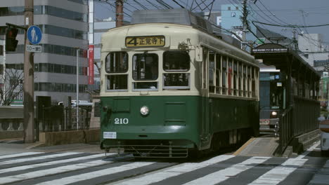 The-Nagasaki-Electric-Tramway-passing-through-shot-followed-by-cars-on-asphalt-road,-Japan