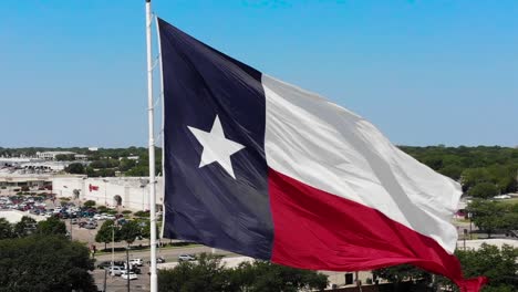 A-close-up,-moving-away,-drone-shot-of-the-texas-flag-with-a-bright-blue-sky-and-a-glimpse-of-Wacos-city-in-the-background
