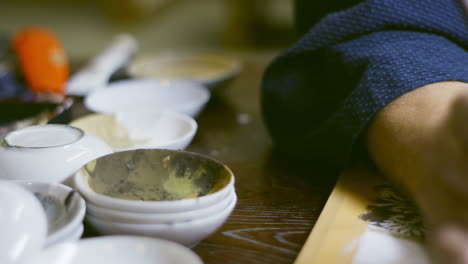 Artist-using-brush-to-mix-colors-in-small-white-ceramic-bowls-in-Kyoto,-Japan