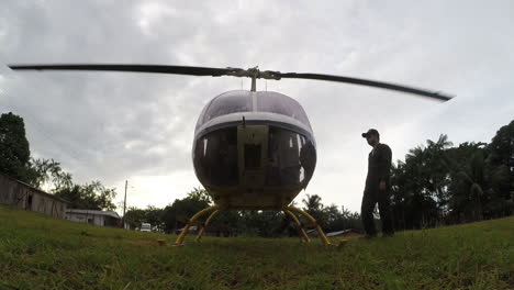 Man-in-dark-green-uniform-get-in-a-helicopter-with-running-engine,-spinning-blades