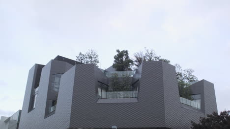 Toma-Estática-De-Un-Edificio-Moderno-En-Tokio-Con-Un-Exuberante-Jardín-En-La-Azotea-Frente-Al-Cielo-Nublado.
