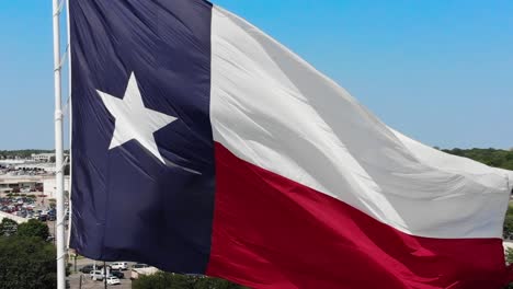 Un-Primer-Plano-De-La-Bandera-De-Texas-Con-Un-Cielo-Azul-Brillante-Y-Un-Vistazo-De-La-Ciudad-De-Wacos-Al-Fondo