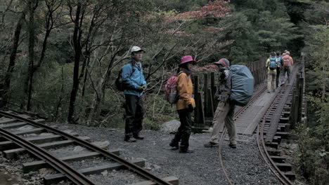 Groups-of-Asian-tourists-walking-across-rail-lines---bridge-in-woodland-trail-environment,-Kyoto,-Japan