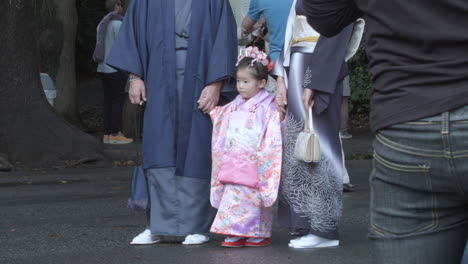 Kleines-Japanisches-Kind-In-Traditioneller-Kimono-Kleidung-Steht-Still-Mit-Zwei-Erwachsenen,-Während-Menschenmengen-Zuschauen