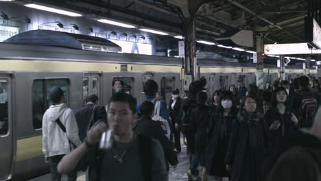 Panning-shot-across-busy-Tokyo-rail-station-as-passengers---commuters-arriving---boarding-as-trains-arrive---depart-platforms