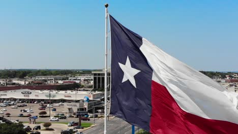 A-close-up-drone-shot,pan-and-tilt-motion-combined,-of-the-texas-flag-with-a-bright-blue-sky-and-a-glimpse-of-Wacos-city-in-the-background