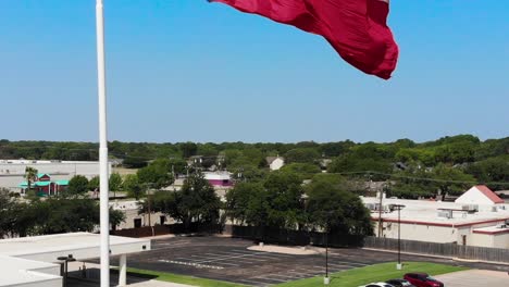 A-close-up-drone-shot,downward-pedestal-motion,-of-the-texas-flag-with-a-bright-blue-sky-and-a-glimpse-of-Wacos-city-in-the-background